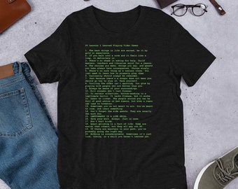 Puede incluir: Una camiseta gris oscuro jaspeada con un diseño de texto verde que enumera 20 lecciones aprendidas jugando a videojuegos. El texto incluye frases como "Las mejores cosas de la vida se ganan", "La curiosidad siempre debe ser recompensada" y "La cartografía es una habilidad para la vida".