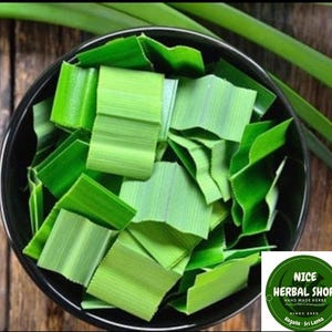 Puede incluir: Un taz&oacute;n negro lleno de hojas de Pandan verdes picadas. Las hojas est&aacute;n dispuestas en un patr&oacute;n aleatorio. El taz&oacute;n est&aacute; sobre una superficie de madera. El texto "NICE HERBAL SHOP" es visible en la esquina inferior derecha de la imagen.