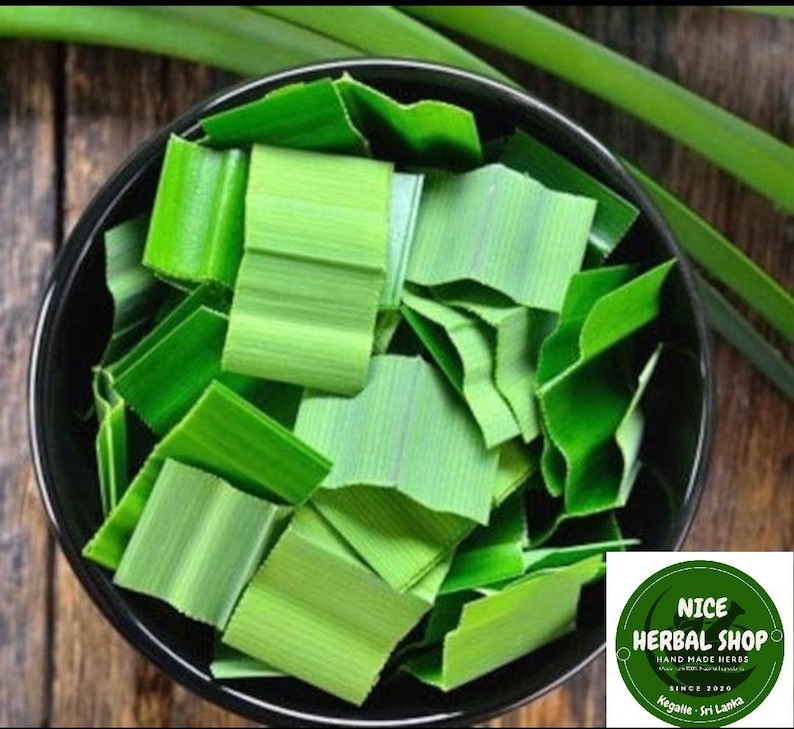 Puede incluir: Un taz&oacute;n negro lleno de hojas de Pandan verdes picadas. Las hojas est&aacute;n dispuestas en un patr&oacute;n aleatorio. El taz&oacute;n est&aacute; sobre una superficie de madera. El texto "NICE HERBAL SHOP" es visible en la esquina inferior derecha de la imagen.