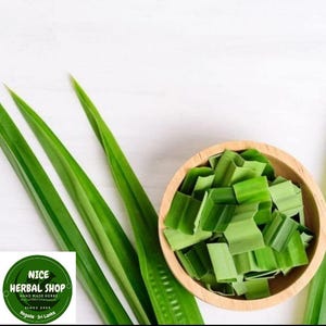 Puede incluir: Un taz&oacute;n de madera lleno de hojas de pandan verdes picadas. Las hojas est&aacute;n dispuestas en una pila y son de un verde brillante. Hay tres hojas largas de pandan verdes en el fondo.