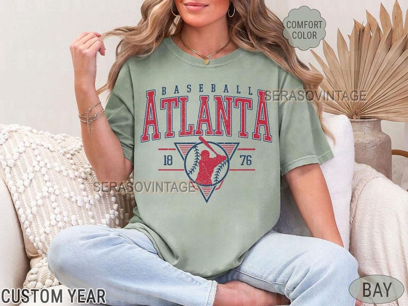 May include: A green t-shirt with a vintage baseball graphic. The graphic features a baseball player in a red silhouette with the text "Baseball Atlanta 18 76".