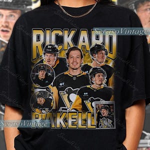 May include: Black t-shirt with a vintage design featuring hockey player Rickard Rakell. The design includes multiple images of the player, the name "RAKELL" in gold, and the text "Seraso Vintage".