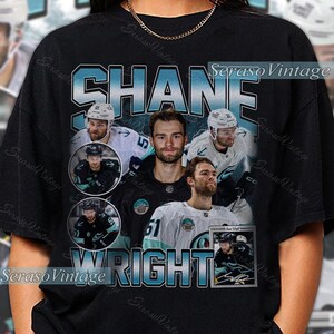 May include: Black t-shirt featuring a collage of hockey player Shane Wright. The design includes the name "SHANE WRIGHT" in a teal font, along with multiple images of the player in action. The shirt has a vintage aesthetic.