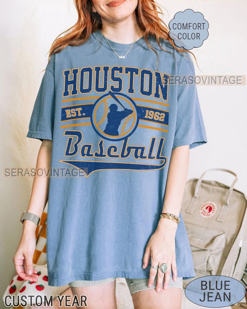 Puede incluir: Una camiseta azul con un gr&aacute;fico de estilo vintage de un jugador de b&eacute;isbol y el texto "Houston Baseball Est. 1962".