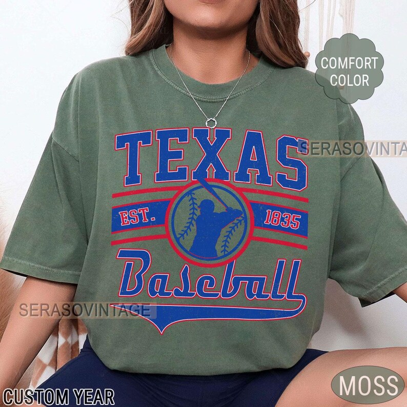 Pode incluir: Uma camiseta verde com um design gr&aacute;fico de estilo vintage que apresenta o texto "Texas Baseball" com uma silhueta de jogador de beisebol e o ano "1835".