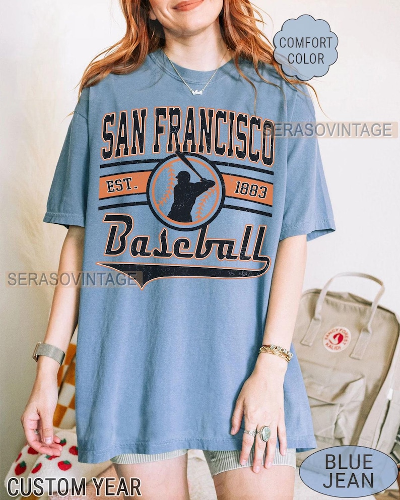 May include: A blue t-shirt with a vintage baseball graphic. The graphic features a baseball player in silhouette, the text "San Francisco Baseball", and the years "Est. 1883".
