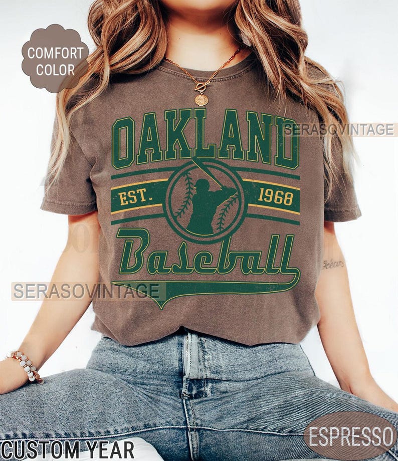 May include: A brown t-shirt with a green and gold graphic that says "Oakland Baseball Est. 1968".