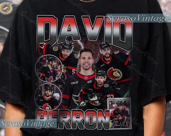 May include: Black t-shirt featuring a graphic of hockey player David Perron. The design includes the name "DAVID" in large letters, player images, and the name "PERRON". The shirt has a vintage aesthetic.