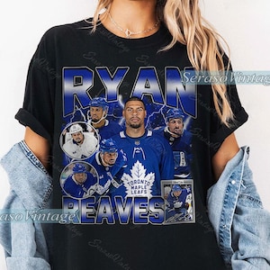 May include: Black t-shirt with a graphic of Ryan Reaves, a Toronto Maple Leafs hockey player. The design includes the player's name, team logo, and action shots. The shirt has a vintage aesthetic.