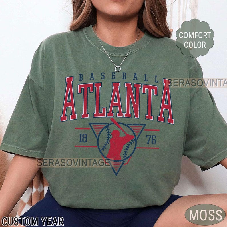 May include: A green t-shirt with a vintage baseball design. The design features a baseball player in a red silhouette, a baseball, and the text "BASEBALL ATLANTA 18 76".
