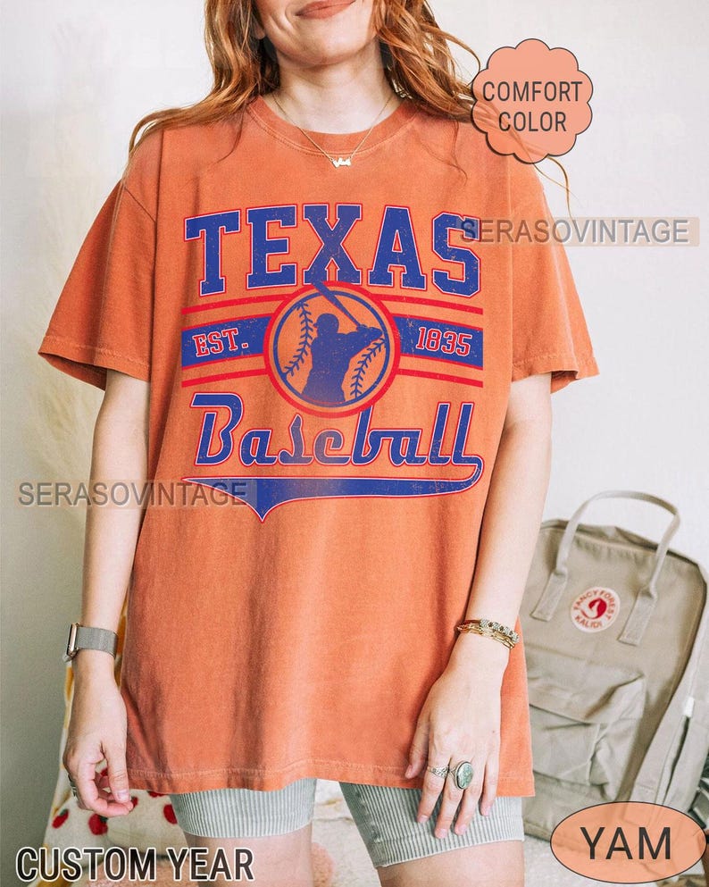 Pode incluir: Uma camiseta laranja queimada com um gr&aacute;fico de beisebol vintage. O gr&aacute;fico apresenta um jogador de beisebol em silhueta, uma bola de beisebol e o texto "Texas Baseball Est. 1835".
