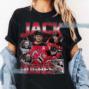 May include: Black t-shirt featuring a vintage-style design with the name "JACK HUGHES" in red and white. The shirt includes images of a hockey player in a red and black uniform. The text "SerasoVintage" is also visible.