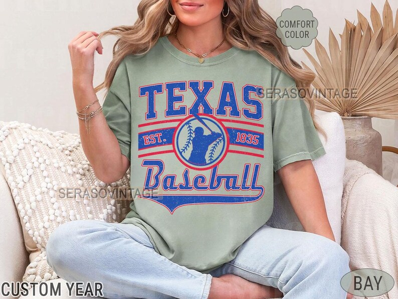 Pode incluir: Uma camiseta verde claro com um design gr&aacute;fico de estilo vintage que apresenta o texto "Texas Baseball" com uma silhueta de jogador de beisebol e o texto "Est. 1935".