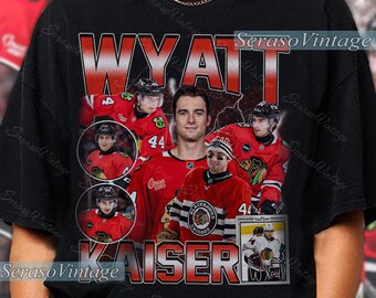 May include: Black t-shirt featuring a graphic of hockey player Wyatt Kaiser. The design includes the player's name, jersey number, and images of him in his team's uniform. The team's logo is also visible.