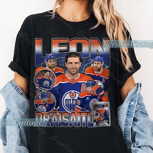 Könnte beinhalten: Schwarzes T-Shirt mit einem Vintage-Grafikdesign von Eishockeyspieler Leon Draisaitl. Das Design zeigt den Namen "LEON" in großen Buchstaben und mehrere Bilder des Spielers in seinem Trikot. Das Teamlogo ist ebenfalls sichtbar.