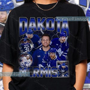 May include: Black t-shirt featuring a collage of hockey player images in blue and white, with the name "DAKOTA MERMIS" in a blue, distressed font. The number 36 is prominent. The shirt has a vintage aesthetic.