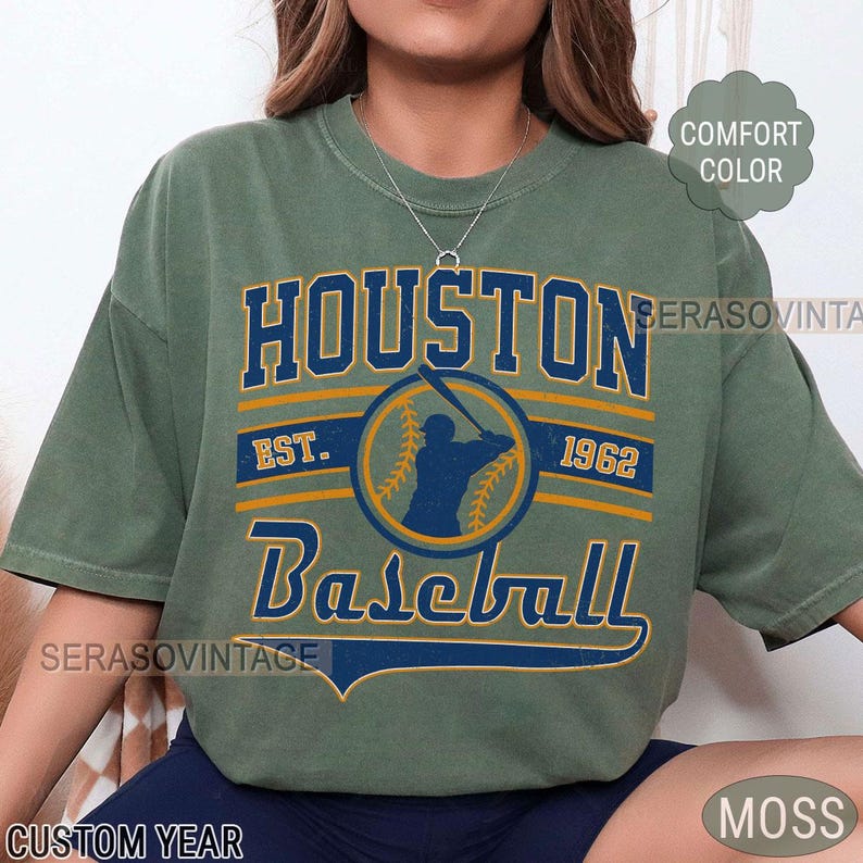 Puede incluir: Camiseta verde con un gr&aacute;fico de estilo vintage de un jugador de b&eacute;isbol en un c&iacute;rculo con el texto "HOUSTON" arriba y "Baseball" abajo. El texto "EST. 1962" est&aacute; dentro del c&iacute;rculo.