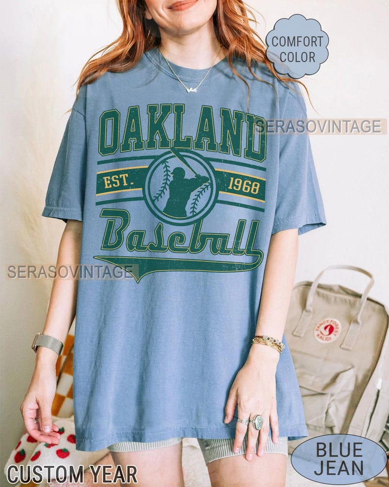 May include: A blue t-shirt with a vintage Oakland Baseball logo. The logo features a baseball player in silhouette, the words "Oakland Baseball", and the years "Est. 1968".