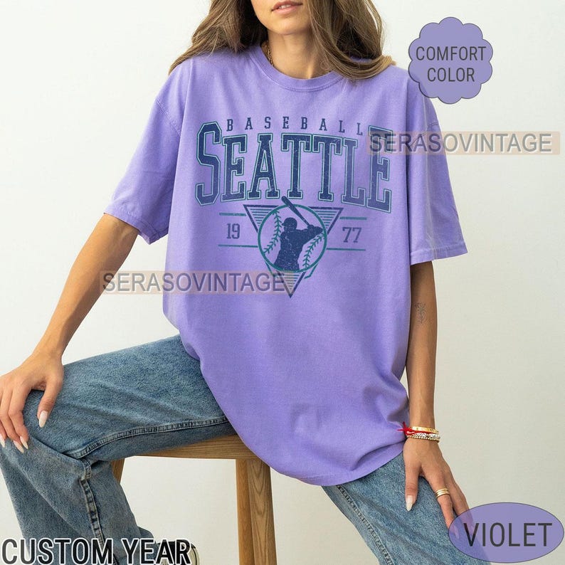 May include: A purple t-shirt with a vintage baseball graphic that says "Baseball Seattle 19 77".