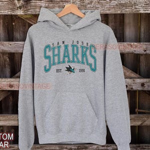 May include: A gray hooded sweatshirt with the San Jose Sharks logo and the text "San Jose Sharks Est. 1991".