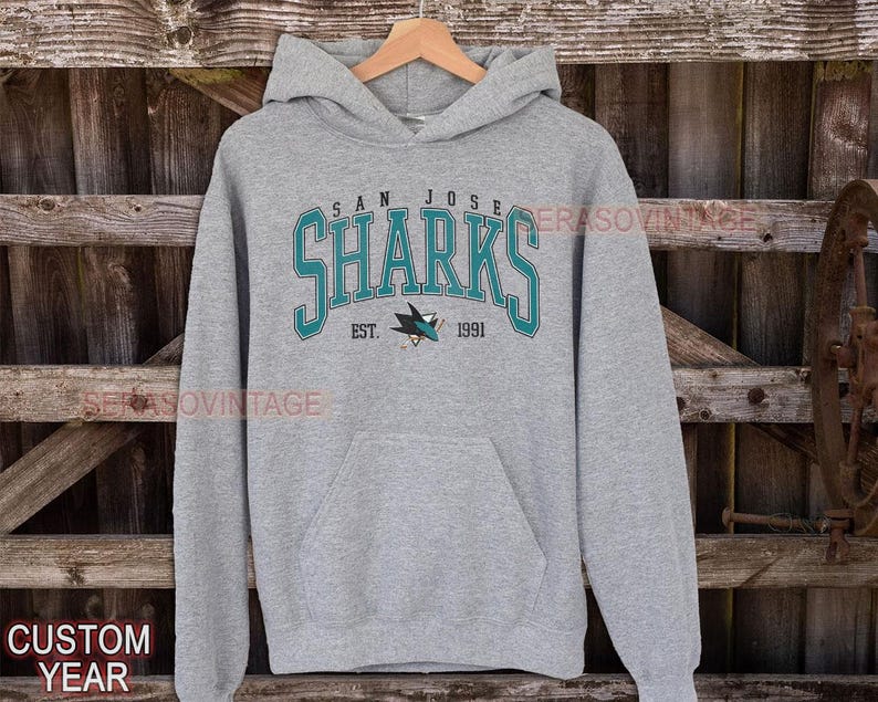 May include: A gray hooded sweatshirt with the San Jose Sharks logo and the text "San Jose Sharks Est. 1991".