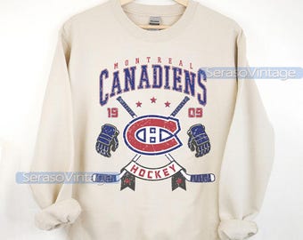 Puede incluir: Una sudadera beige con un logotipo vintage de hockey de los Montreal Canadiens. El logotipo incluye el nombre del equipo, un palo de hockey, un disco y los años 1909 y 09. El texto "Hockey" está impreso debajo del logotipo.