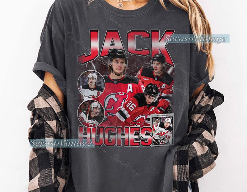 May include: Dark gray t-shirt featuring a graphic of hockey player Jack Hughes. The design includes the name "JACK HUGHES" in red, with images of the player in action. The shirt has a vintage, distressed look.