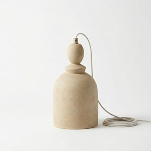 Op de afbeelding: Een beige hanglamp met een klokvormige basis en een afgeronde bovenkant. De lamp hangt aan een grijs snoer. De lamp heeft een getextureerd oppervlak en een neutraal kleurenpalet. Hoogte: ongeveer 30 cm.
