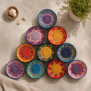 Puede incluir: Una colección de diez platos ralladores circulares de cerámica dispuestos en triángulo. Cada plato presenta una superficie de rallado central texturizada rodeada por un colorido patrón floral en tonos azul, rojo, amarillo, morado y verde.