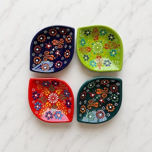 May include: Four leaf-shaped ceramic bowls featuring intricate hand-painted floral patterns. The set includes one dark blue, one lime green, one bright red, and one dark teal bowl, each decorated with colorful dots and swirling motifs.