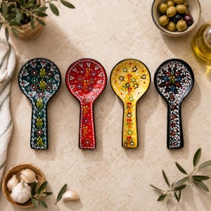 May include: Four ceramic spoon rests arranged in a row, each featuring a distinct background color of dark green, red, yellow, and black. Every spoon rest is decorated with intricate, colorful floral patterns and raised dot details.