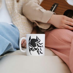 May include: A white ceramic mug with a black silhouette of Batman's head with bats flying around it.