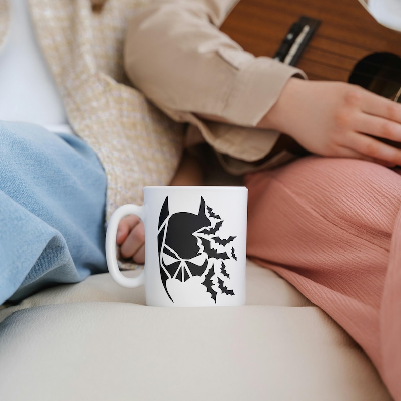 May include: A white ceramic mug with a black silhouette of Batman's head with bats flying around it.