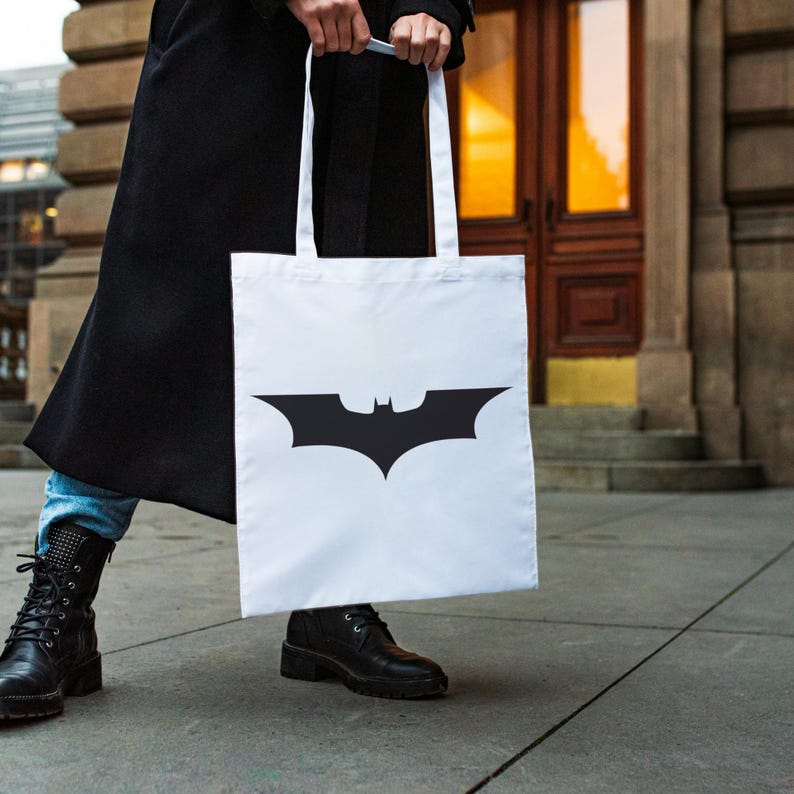 May include: A white tote bag with a black Batman logo. The bag has two handles and is made of a sturdy fabric.