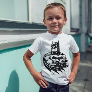 May include: A white t-shirt with a black and white illustration of Batman on the front. The shirt is being worn by a young boy.