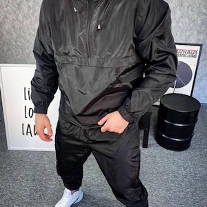 May include: A black tracksuit with a zippered jacket and matching pants. The jacket has a hood and a half-zip closure. The pants have an elastic waistband and a drawstring.