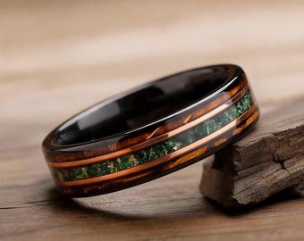 May include: A black ring with a wood grain and green stone inlay. The ring has a polished finish and is displayed on a piece of wood. The ring is a piece of jewelry.