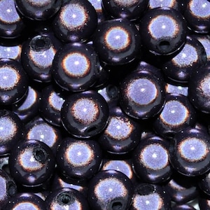 Peut inclure: Gros plan sur un groupe de perles irisées violettes et noires. Les perles ont une finition mouchetée et scintillante et un petit trou au centre.