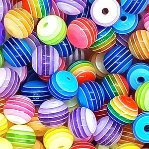 Könnte beinhalten: Eine Sammlung bunter, runder Perlen mit Streifen. Die Perlen sind aus Kunststoff und haben eine glänzende Oberfläche. Sie sind perfekt zum Basteln und für die Schmuckherstellung.