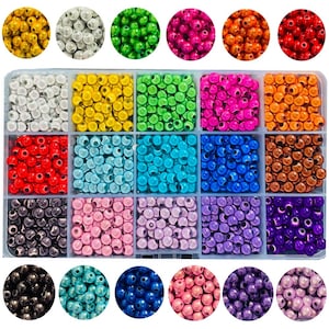 Op de afbeelding: Assortiment van 24 kleine ronde kralen in verschillende kleuren, waaronder goud, zilver, rood, groen, blauw, paars en bruin. De kralen zijn gerangschikt in een plastic bakje met 12 vakjes.