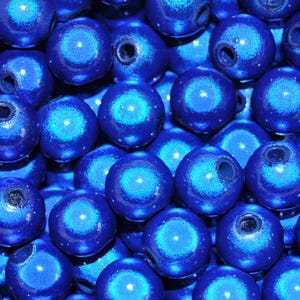 May include: A close-up shot of numerous deep blue, spherical beads. Each bead has a glossy surface with a lighter blue, swirling design in the centre. The beads are closely arranged, filling the entire frame.
