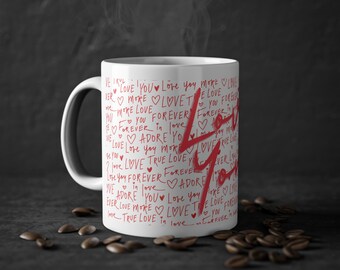 Può includere: Tazza in ceramica bianca con un designo rosso che dice "Ti amo" più volte. Il design è in stile calligrafico con cuori.