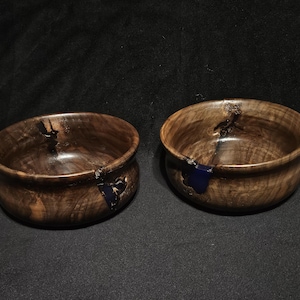 May include: Two wooden bowls with dark brown wood and blue resin accents. The bowls are round and have a slight curve to them.