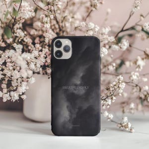 Könnte beinhalten: Schwarze Smartphone-Hülle mit Wolkenmuster und dem weißen Schriftzug "BREATHE DEEPPLY". Die Hülle hat eine matte Oberfläche und einen Kameraausschnitt. Die Handyhülle ist von weißen Blumen umgeben.