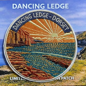 May include: A circular embroidered patch featuring a coastal landscape with a sunrise over the sea, rocky cliffs, and the text DANCING LEDGE - DORSET. The design uses shades of orange, yellow, blue, and brown thread with a white stitched border.