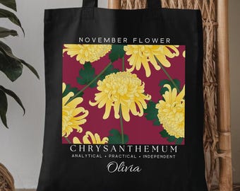 May include: Black tote bag featuring a floral design with yellow chrysanthemums on a burgundy background. The text "NOVEMBER FLOWER" and "CHRYSANTHEMUM" are printed above and below the floral design, with the name "Olivia" at the bottom.