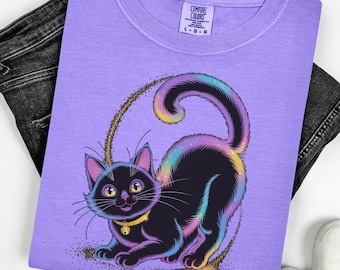 May include: A lilac Comfort Colors t-shirt featuring a black cat with a rainbow-colored tail and accents. The cat is inside a gold glitter circle. The shirt is paired with black jeans and white sneakers.