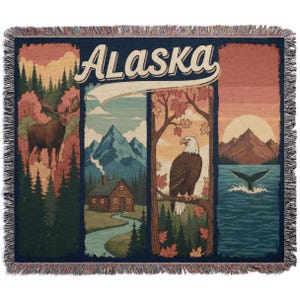 May include: A woven throw blanket with a vintage design, featuring the word "Alaska". The design includes a moose, mountains, a cabin, an eagle, and a whale tail. The blanket has a fringed edge, and is suitable for a sofa or bed.