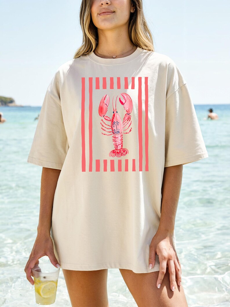 Cream t-shirt with a pink lobster design and vertical stripes.