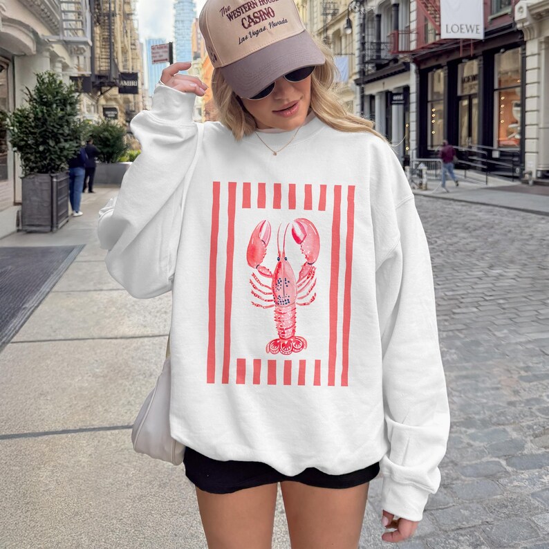White crewneck sweatshirt with a watercolor lobster graphic on red and white stripes.